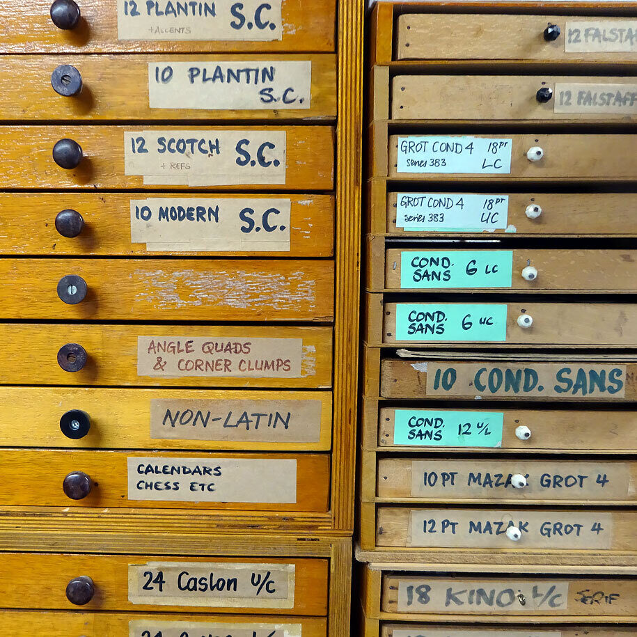 Detail of the front of several small cabinets full of metal type; assorted typefaces.